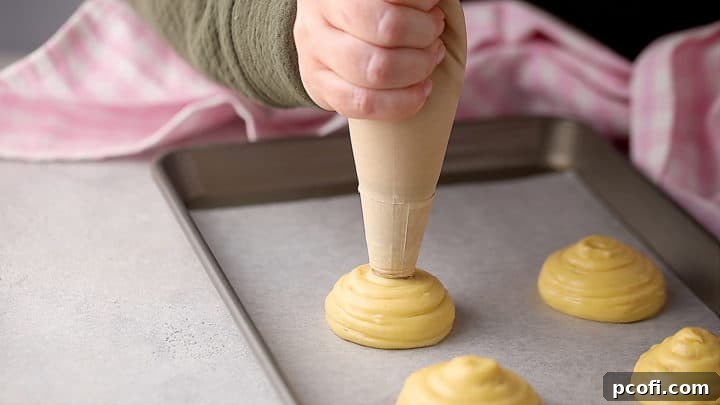 Piping rounded portions of pâte à choux onto a baking sheet with a pastry bag.