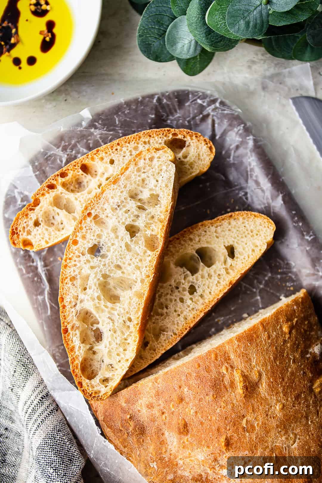 Overhead image of a ciabatta roll cut into slices, with olive oil & balsamic nearby for dipping.