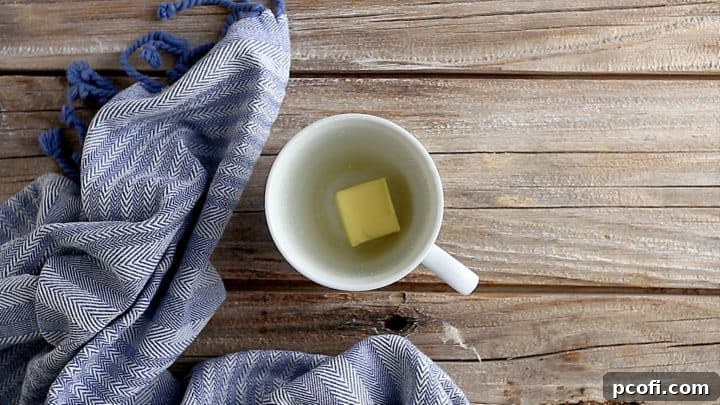 Two tablespoons of butter in the bottom of a coffee mug, ready to be melted.