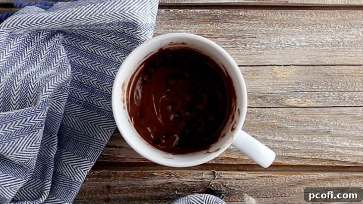 Unbaked chocolate mug cake batter topped with chocolate chips in a white ceramic mug.