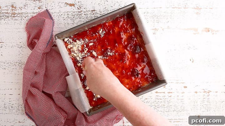 Sprinkling the buttery crumb topping generously over the sweet jam layer of the bars.