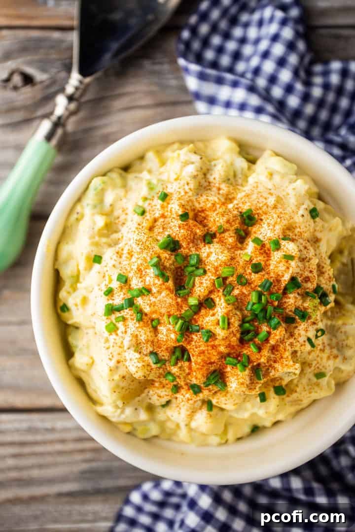 Overhead image of a bowl of potato salad on a weathered wood tabletop, with a serving spoon alongside, ready for a meal.