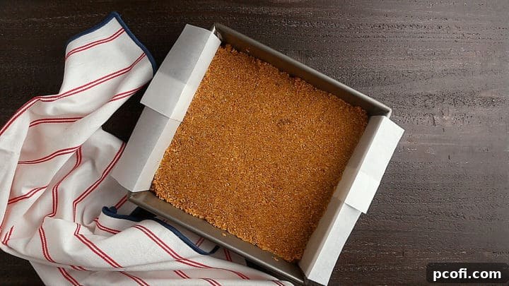 Smooth, even layer of graham cracker crust pressed into a square baking pan, ready for the next layer.