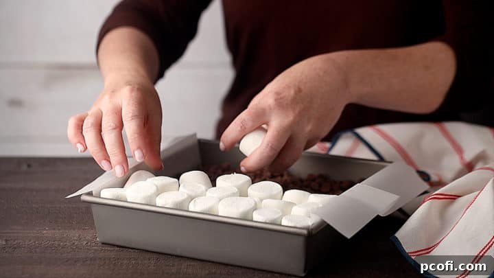 Placing marshmallows over the chocolate chip layer in a baking pan, ready for toasting.