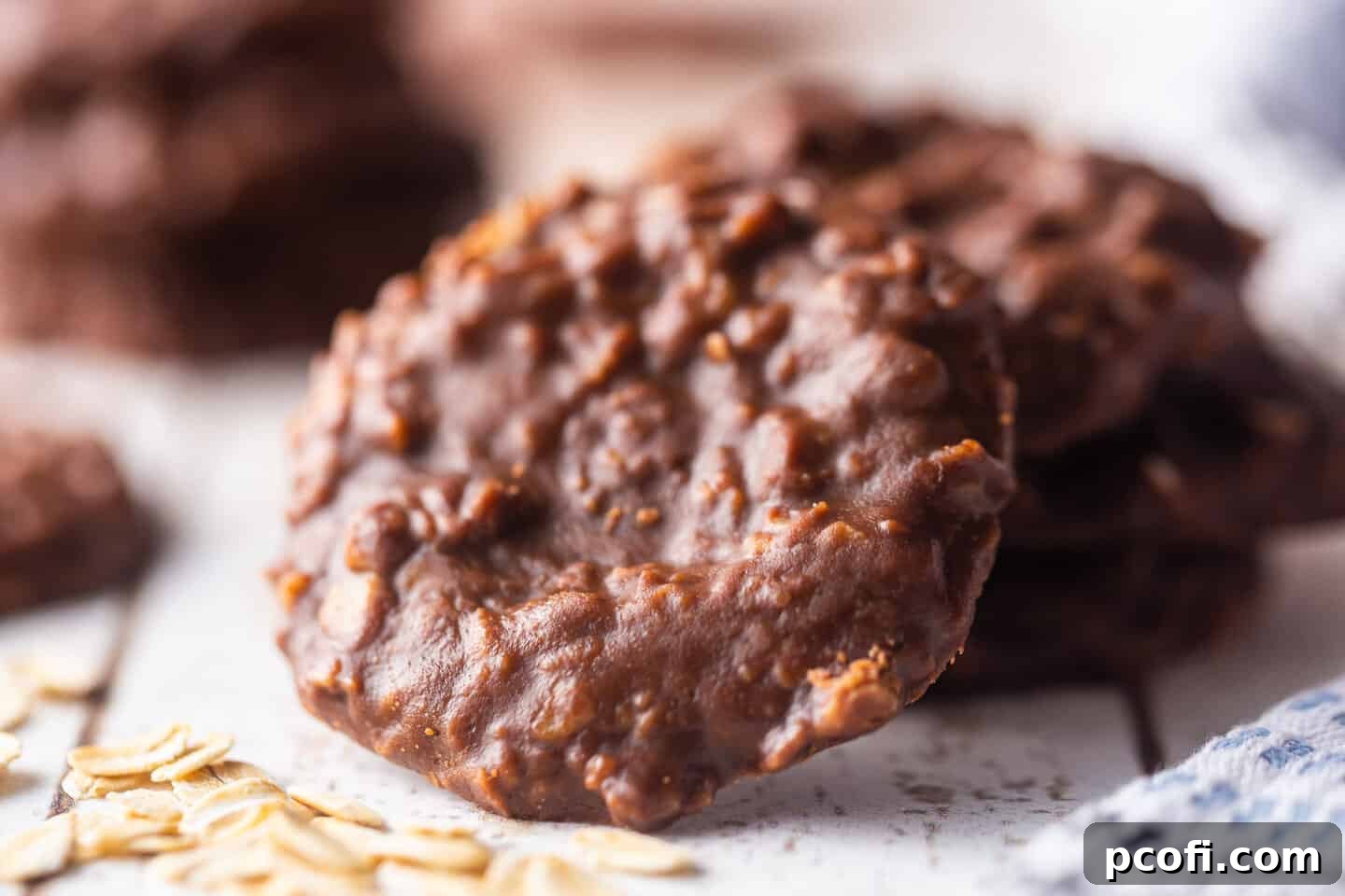 Close-up, horizontal view of rich chocolate oatmeal no-bake cookies, with visible oats, scattered on a surface.