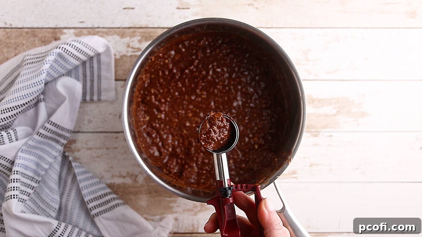 A scoop of no-bake cookie mixture being dropped onto a parchment-lined baking sheet.