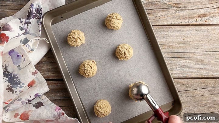 Scooping brown sugar cookie dough onto a parchment-lined baking sheet.