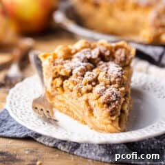 Slice of Dutch apple pie on a white eyelet plate with a grey plaid napkin.