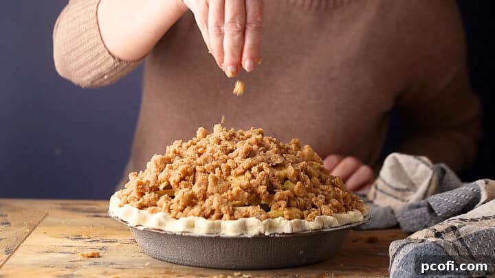 Sprinkling crumb topping over Dutch apple pie, creating an even, golden layer.