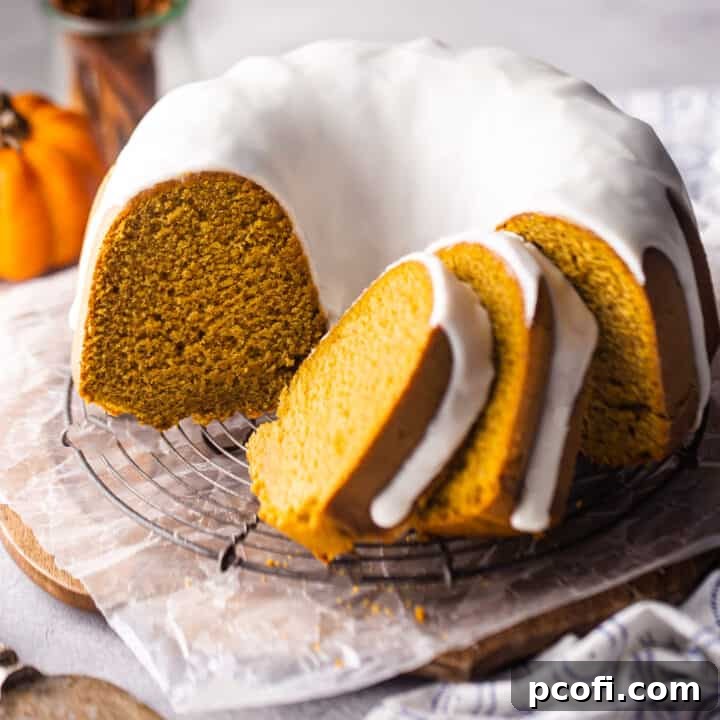 Pumpkin bundt cake with cream cheese glaze sliced and presented on a wire rack.