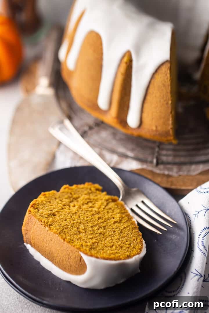 Slice of pumpkin spice bundt cake served on a dark blue plate, with the whole cake in the background.