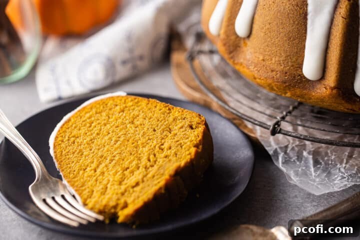 Close up of a slice of pumpkin cream cheese bundt cake on a dark plate with a vintage silver fork.