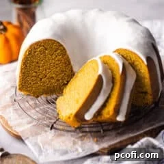Pumpkin bundt cake with cream cheese glaze sliced and presented on a wire rack.