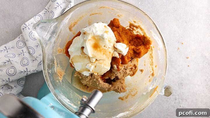 Adding pumpkin puree, sour cream, and vanilla to pumpkin cake batter.