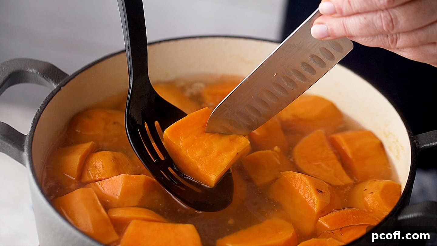 Fork tender boiled sweet potatoes in a large pot of salted water, ready for mashing.