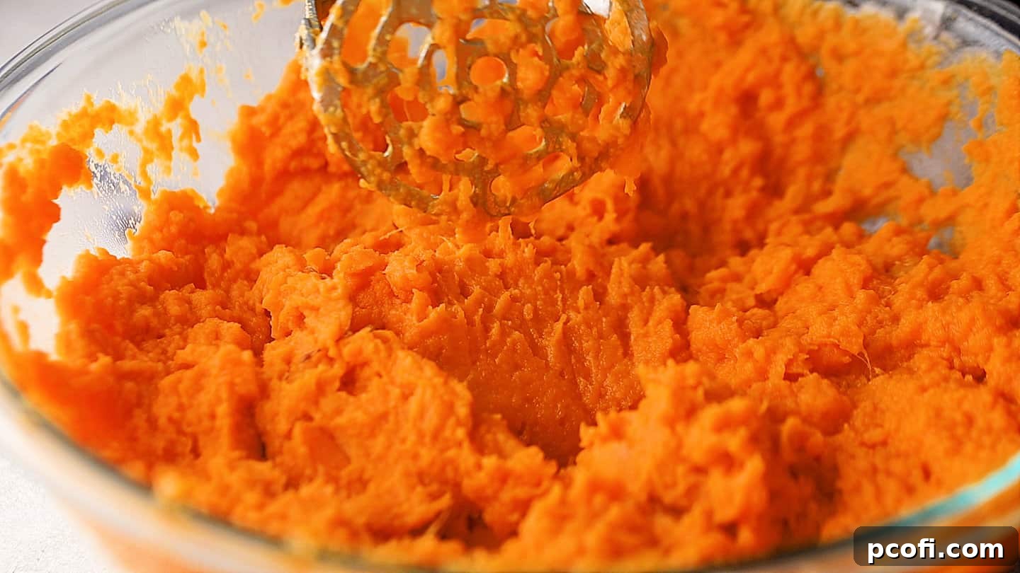 Mashed sweet potatoes in a large glass mixing bowl, appearing creamy and smooth.