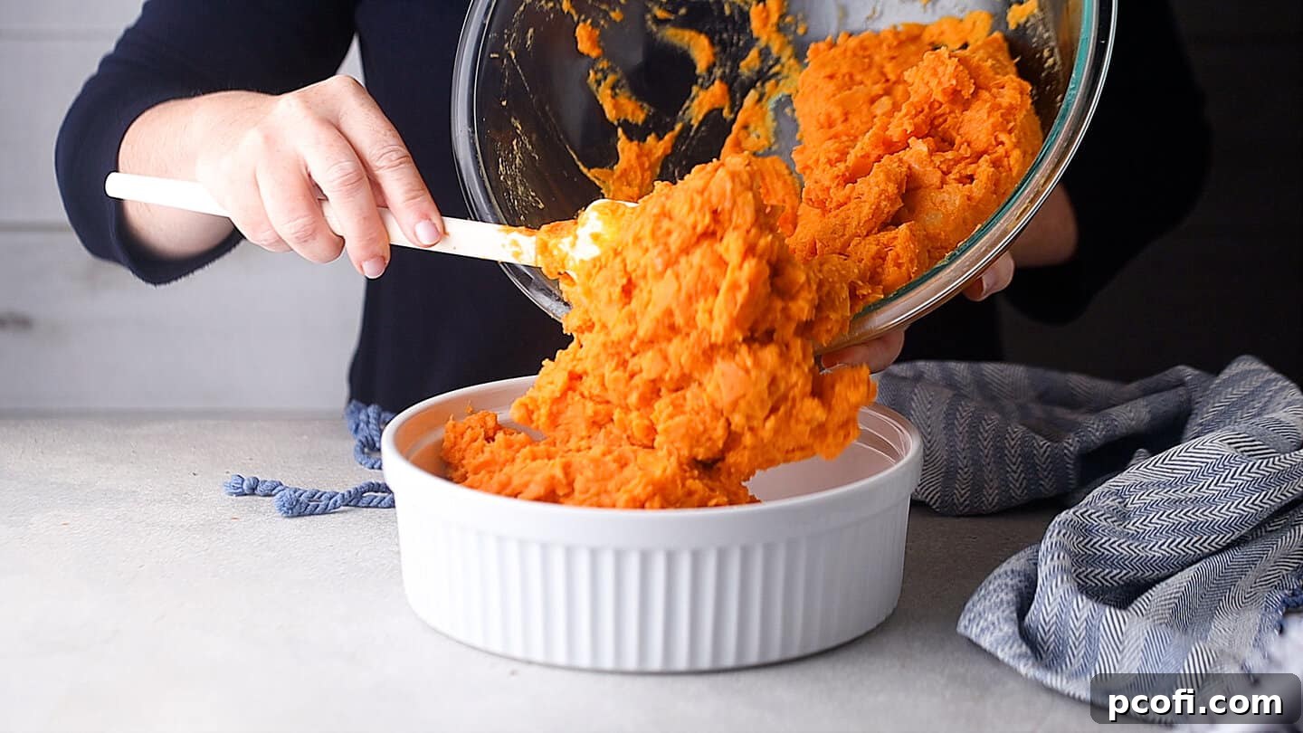 Transferring creamy sweet potato mash into a baking dish before adding topping.