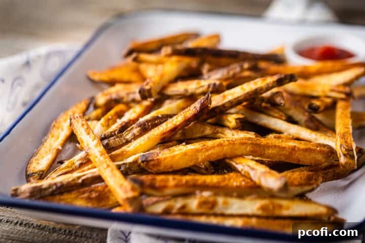 A wooden tabletop showcasing a tray piled high with perfectly golden brown and crispy oven fries, ready to be enjoyed.