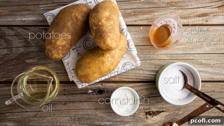 All the core ingredients for making the best crispy oven fries laid out on a rustic wooden table: potatoes, vinegar, salt, oil, and cornstarch.