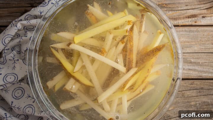 Sliced potato fries soaking in a bowl of hot water with apple cider vinegar and salt.