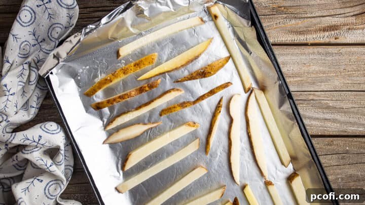 Potato fries arranged in a single, even layer on a hot baking sheet, ready to go into the oven.