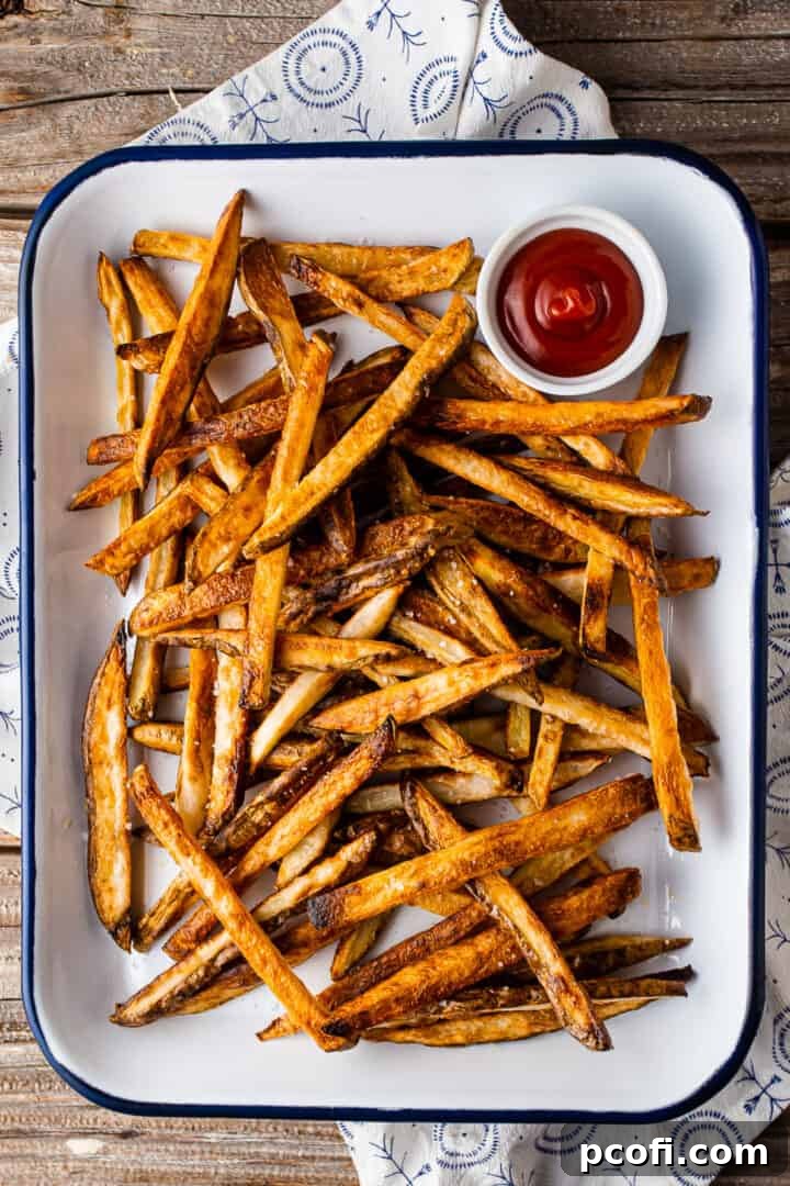 An enamel tray filled with perfectly golden brown baked French fries, accompanied by a blue and white checkered cloth.