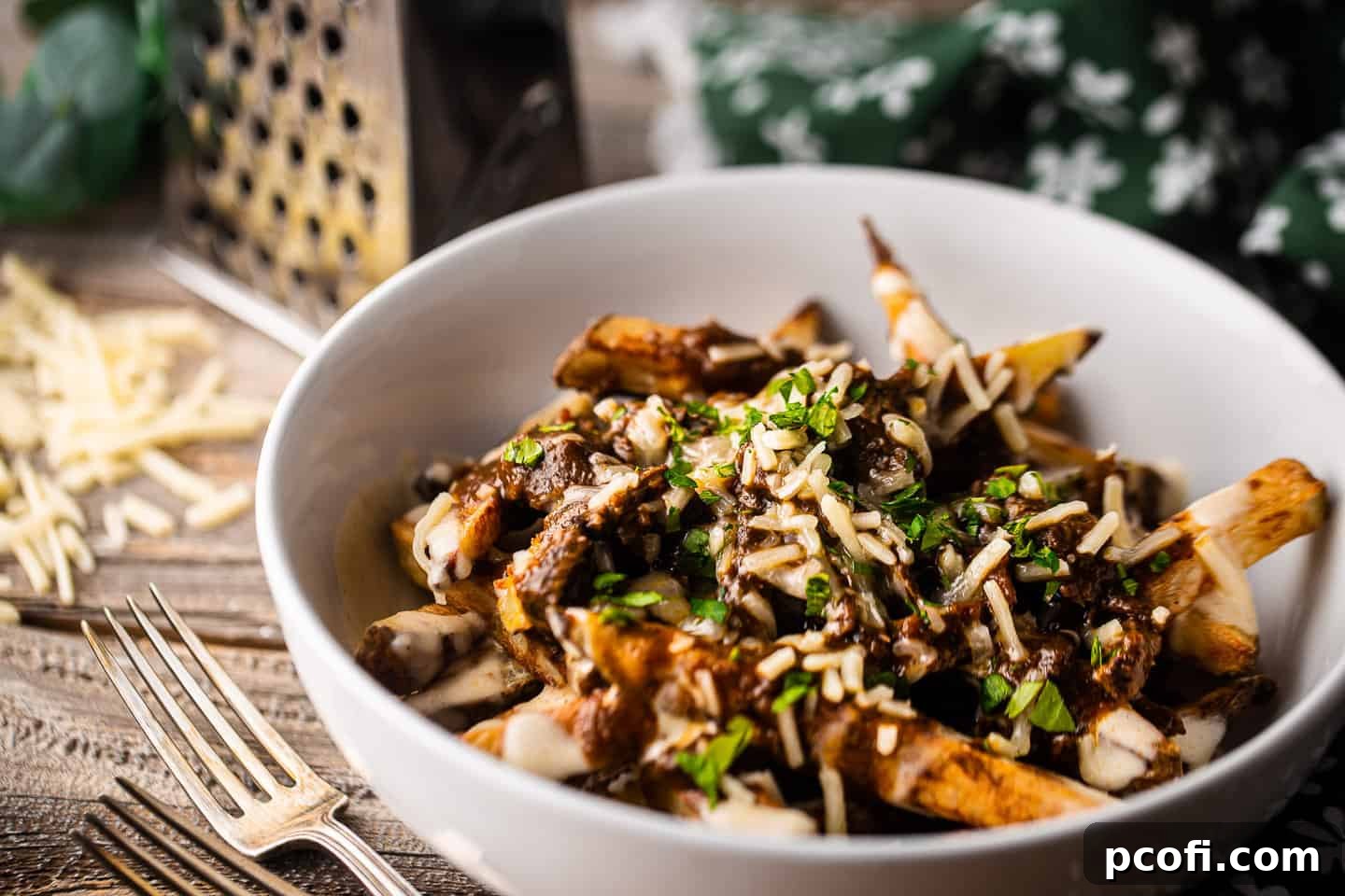 Poutine served in a shallow white bowl with cheese in the background, highlighting the luxurious layers of the dish.