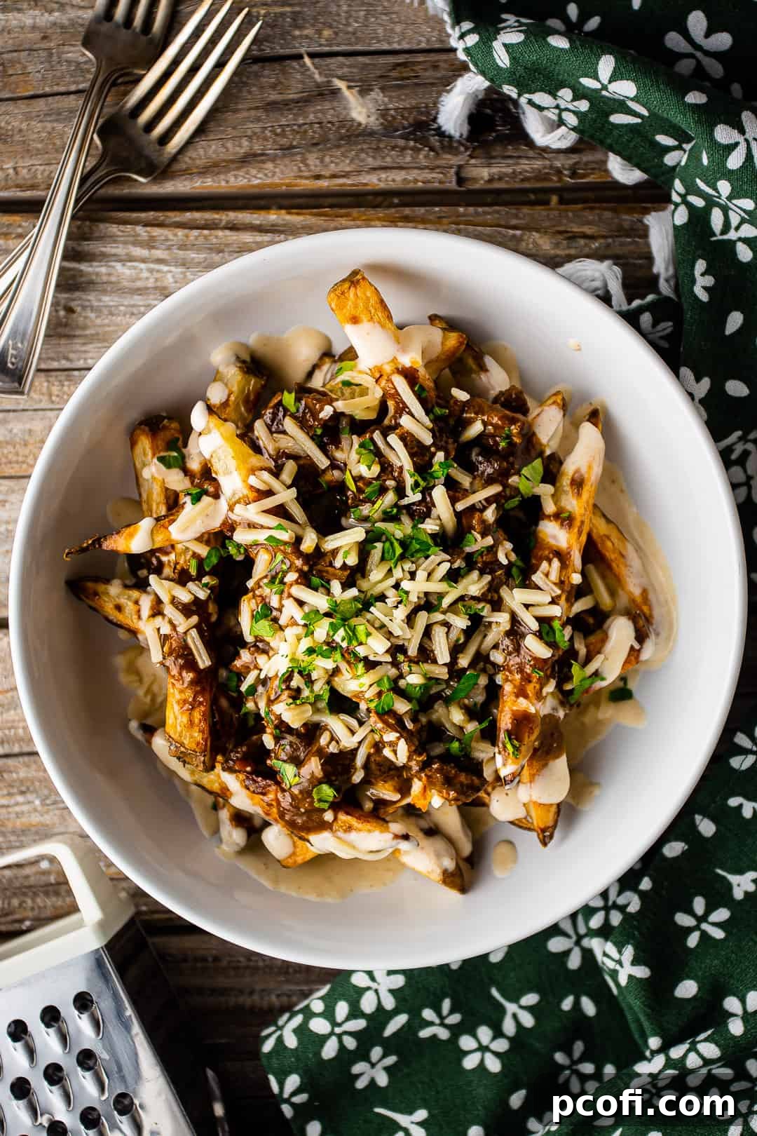 Poutine fries presented in a shallow white bowl with a green floral napkin and vintage silver cutlery.