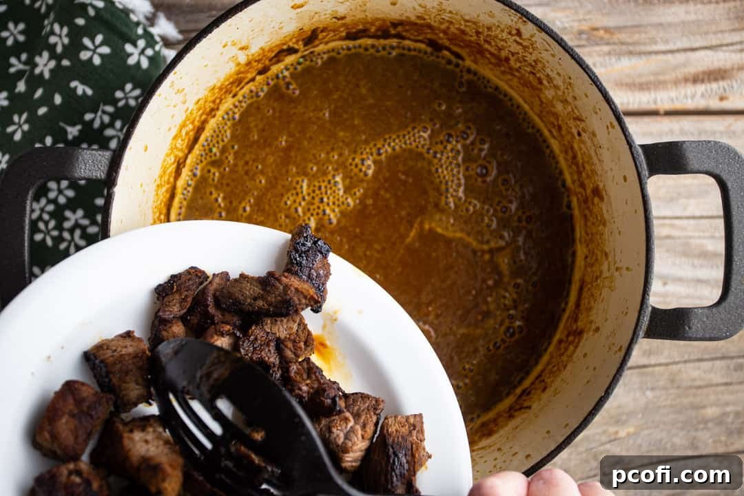Adding browned beef back to the braising liquid for slow simmering until tender.