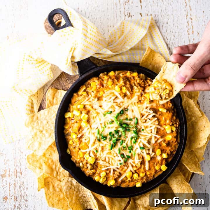 Scooping generous helpings of hot Mexican corn dip from a rustic cast iron skillet with a crispy corn chip, showcasing its creamy, cheesy texture loaded with vibrant vegetables and savory chorizo.
