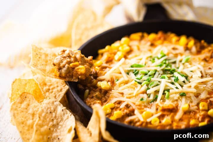 A corn chip laden with a generous scoop of hot Mexican corn dip, showcasing pieces of chorizo, corn kernels, and melted cheese, ready to be enjoyed.