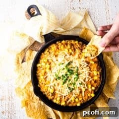 Scooping corn dip from a hot skillet with a corn chip.