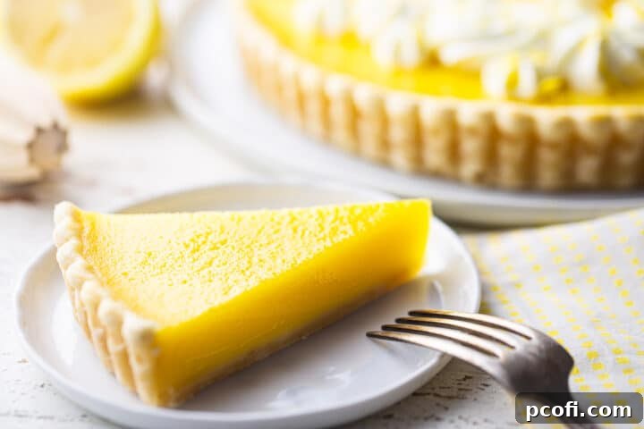 A perfect slice of golden lemon tart, with its creamy filling and buttery crust, served on a plate with a fork, and a lemon reamer in the soft-focus background.