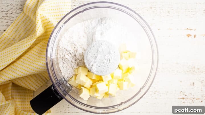 A bowl of dry ingredients for tart crust (flour, powdered sugar, salt) with cubes of cold unsalted butter on top, ready for processing.