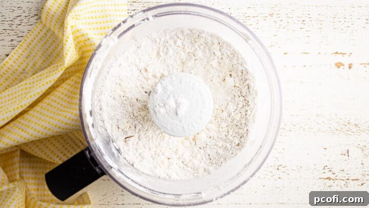 Dry ingredients for tart crust with cold, cubed butter partially cut in, showing a coarse, crumbly texture in the food processor.