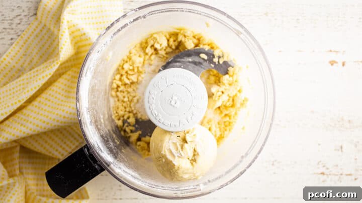 Tart crust dough perfectly formed into a cohesive ball within the bowl of a food processor, cleanly separated from the sides.