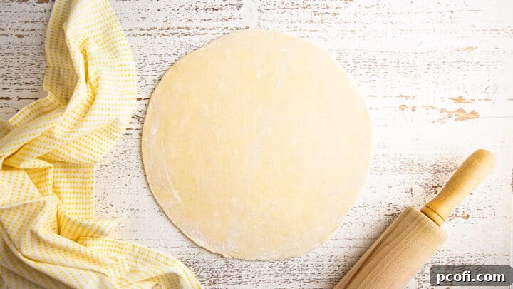 Tart crust dough meticulously rolled out on a floured surface, with its diameter slightly exceeding that of the tart pan, demonstrating readiness for transfer.