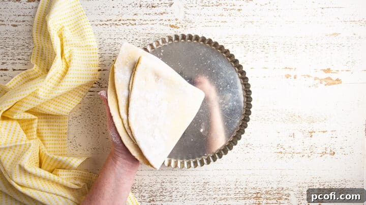 The process of gently transferring the rolled-out tart crust dough into the tart pan, ensuring it covers the bottom and sides.