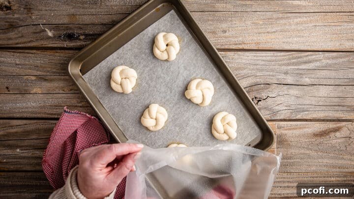Covering unbaked garlic knots with greased plastic wrap.