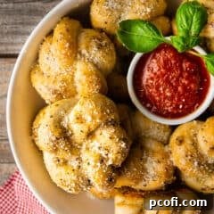 Garlic knots in a bowl with marinara sauce and fresh basil.