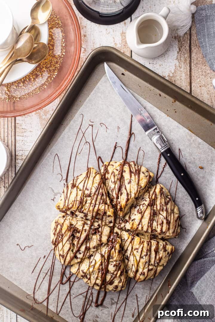 Overhead view of a beautiful breakfast spread featuring chocolate chip scones on a baking sheet, surrounded by coffee cups and plates.