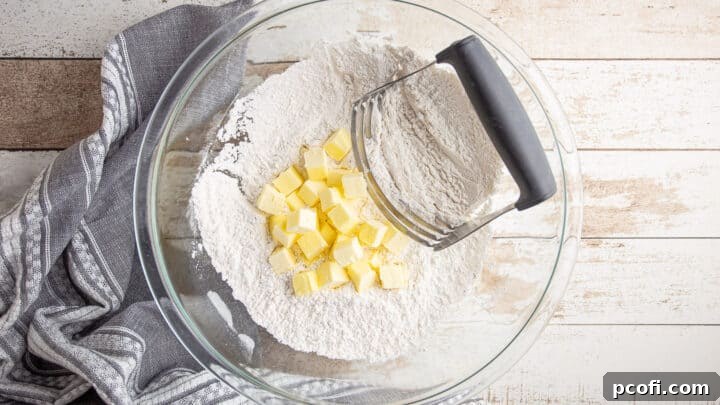 Cubed cold butter added to the dry scone ingredients, with a pastry blender poised to cut it in.