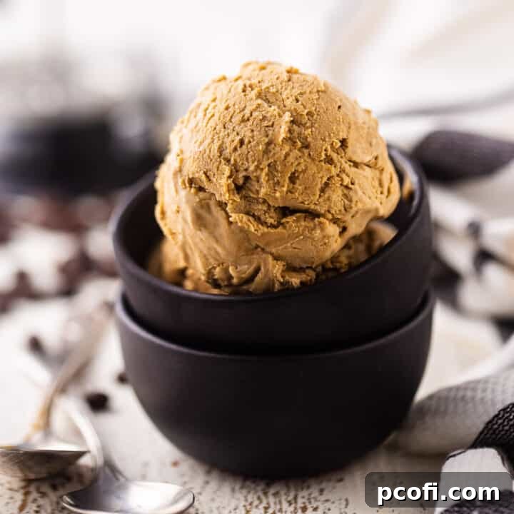 A scoop of rich, creamy no-churn coffee ice cream in a dark brown bowl, surrounded by scattered roasted coffee beans.
