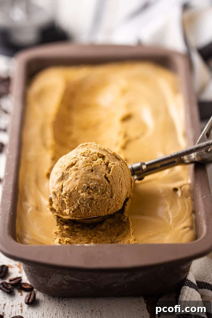 A loaf pan filled with freshly made no-churn coffee ice cream base, with a vintage ice cream scoop resting inside.