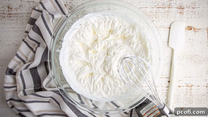 Fluffy peaks of whipped heavy cream in a large glass mixing bowl, ready for the next steps of the no-churn coffee ice cream recipe.