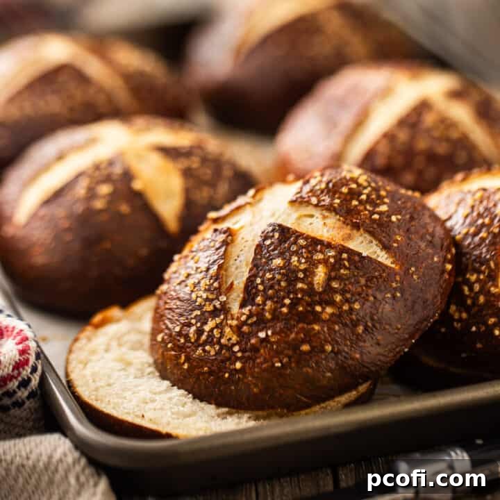 Freshly baked pretzel bun sliced horizontally, showcasing its soft interior, presented on a baking tray.