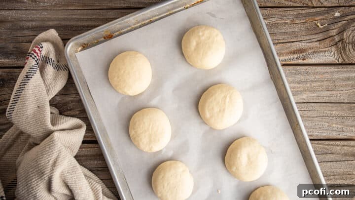 Unbaked pretzel buns, shaped into round disks and placed on a parchment-lined baking sheet, ready for their second rise.