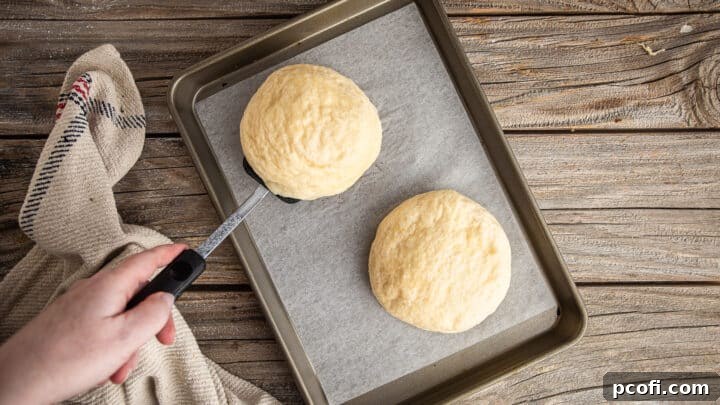 Boiled pretzel buns being drained on a clean towel before being placed onto a parchment-lined baking sheet.