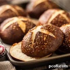 Freshly baked pretzel bun sliced horizontally, showcasing its soft interior, presented on a baking tray.