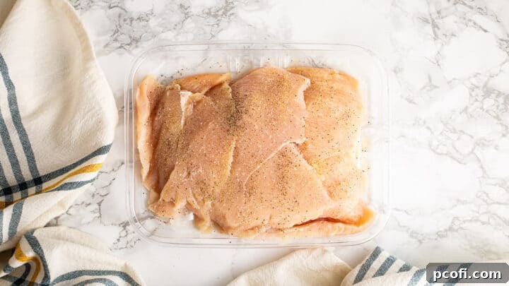 Thin sliced chicken breasts being seasoned with salt, pepper, and garlic powder.